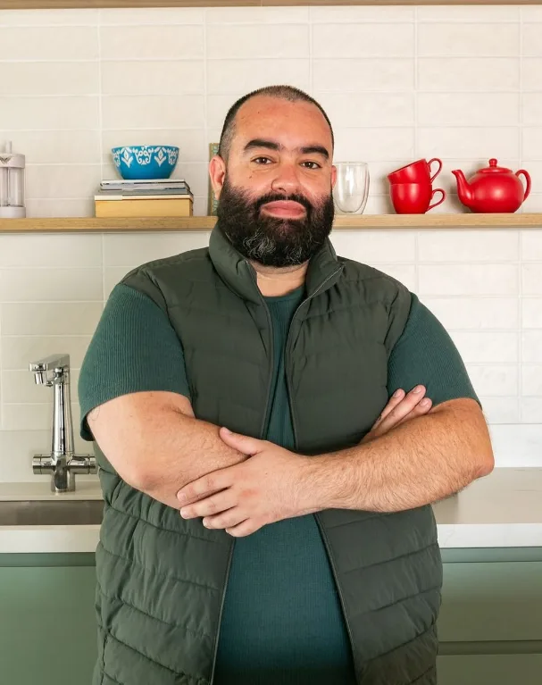 Paulo Capel, de braços cruzados, em uma cozinha com marcenaria verde